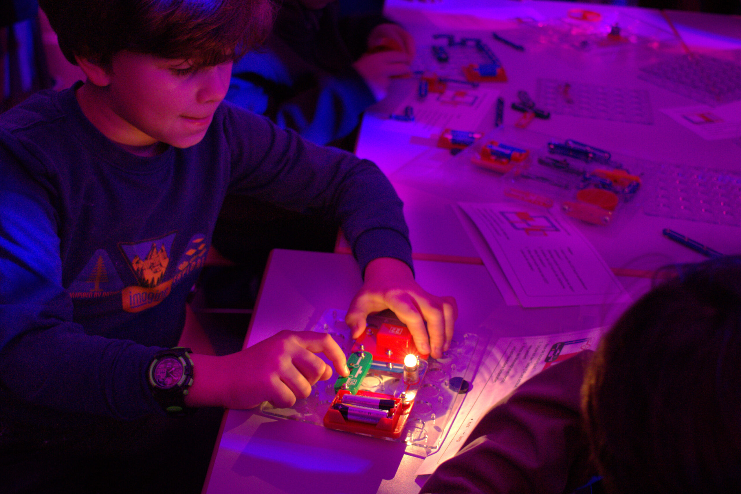 A boy of primary school age operates the switch of a self-made circuit in which a small light bulb lights up
