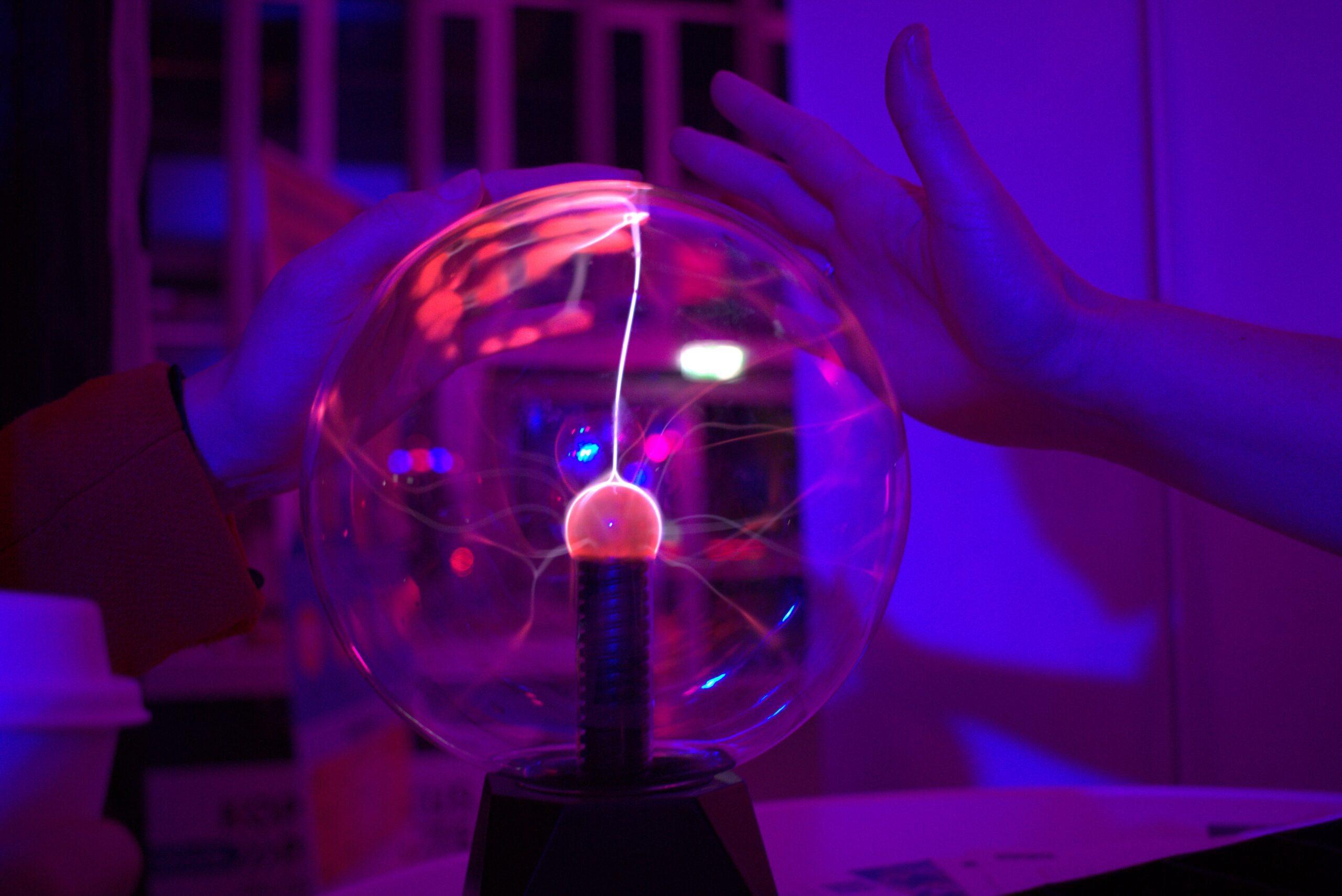 A child's hand touches a plasma ball and makes it glow, while a second hand is about to touch the ball.