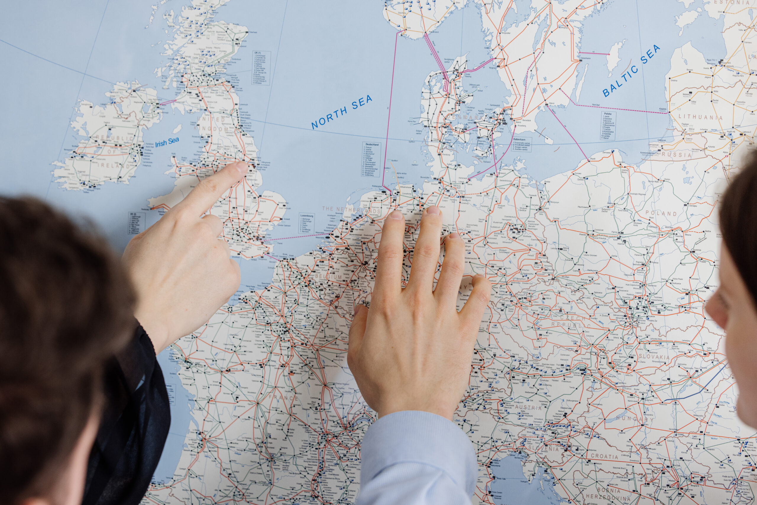 Two hands of different people point to specific points on a map showing the expansion of the electricity grid in Northern Europe and the Baltic region.