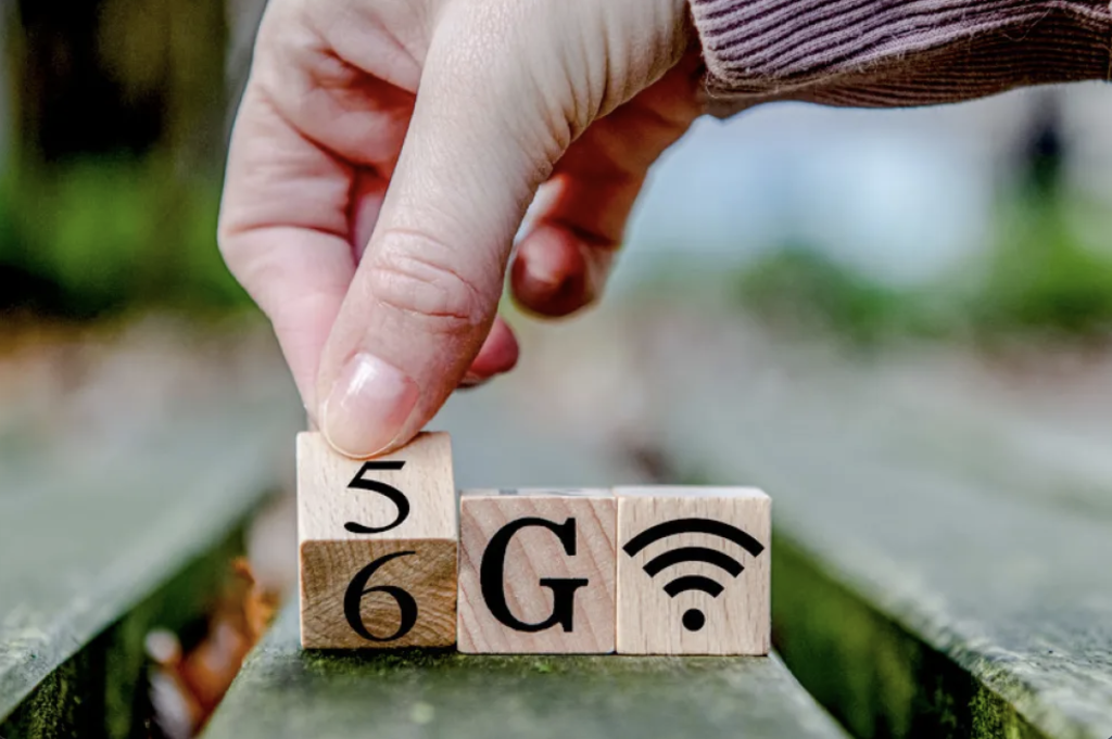 A hand rotates a wooden block from the number 5 to 6 to spell out '6G' next to a Wi-Fi symbol block, symbolizing the transition to the next mobile generation.