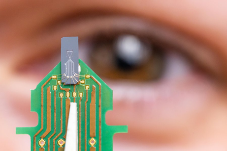 Microchip on tweezers in front of a human eye.