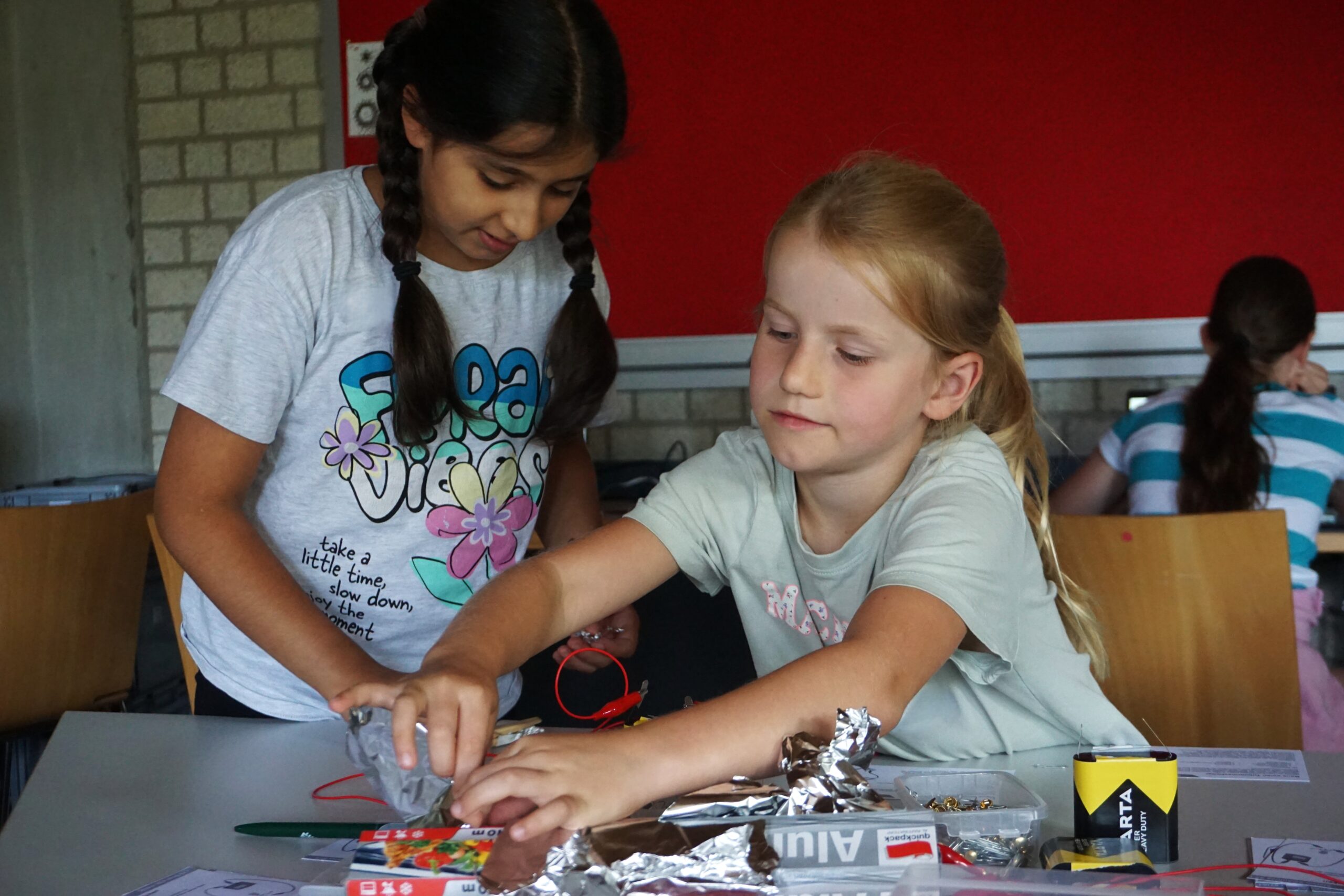 Two young girls are doing crafts with electrical components.