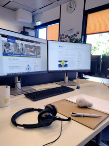 Schreibtisch mit zwei Bildschirmen, Arbeitsutensilien, Kopfhörern, einer Kaffeetasse und Stressbällen zum Tag der Forschungsdaten am 15. November 2022.