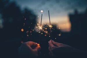 Two hands hold two luminous sparklers