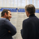 Zwei Personen stehen vor Poster und unterhalten sich