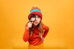Child with magnifying glass in front of orange background