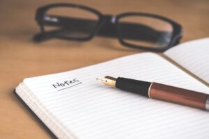 Notebook with a pen and glasses in the background