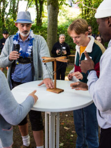 Drei Personen versuchen einen Ring an einer Schnur an einen Haken zu schwingen.