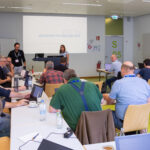 A seminar room with participants at their laptops; at the front, a presenter at the lectern in front of a slide bearing the text “deutsches forschungsnetz.”