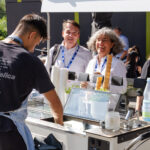 Lachende Personen an einem mobilen Eisstand bei sonnigem Wetter im Freien.